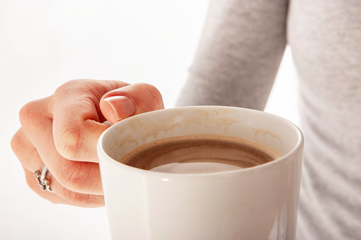 Woman holding cup full of coffee or hot chocolate close-up, white background