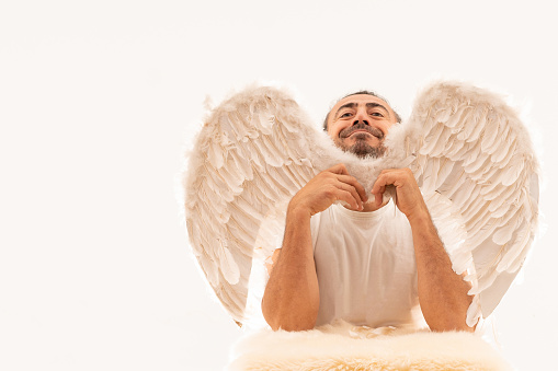 Portrait of a humor man wearing angel wings standing over white background