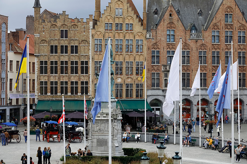 Bruges, Belgium - September 15, 2022: The flags on the masts fly almost in the central part of the Market Square and you can see them here against the background of brick houses surrounding this square