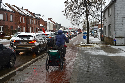 Leuven, Vlaams-Brabant, Belgium - March 8, 2023:cycling woman goes faster than commuter cars in traffic jams this morning because of the snowy asphalt roads