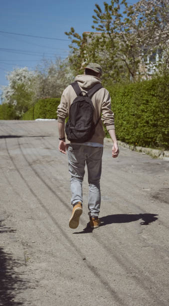 istock View from back. Man tourist in hoodie, cap with backpack goes forward. The guy with a black backpack in a cap, rear view. 1472158718