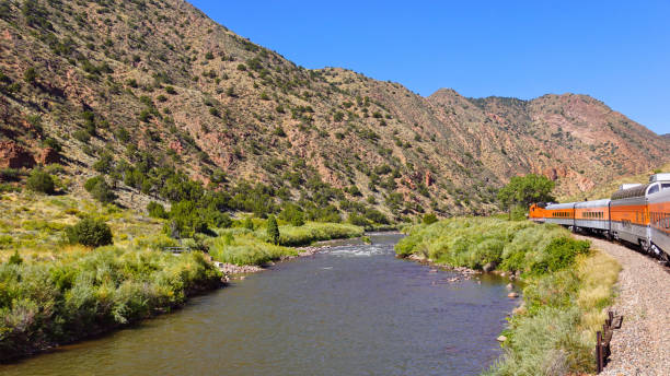 istock Orange Passenger Train Traveling Through a Canyon Next to a River 1472161648