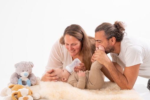 Happy parents feeding their baby boy with milk bottle in bedroom