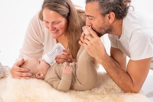 Happy parents feeding their baby boy with milk bottle in bedroom