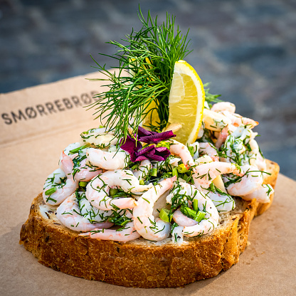 Traditional delicious Danish snack called smørrebrød butter bread, rich adorned with prawns, chives, dill, lemon slices and edible flowers, showcasing the delicacy of Scandinavian food and culture.