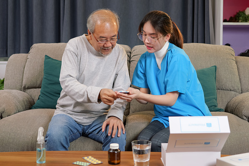 Young doctor examining senior patient at home visit, Senior man consulting medicine with pharmacist, Caregiver nurse taking care of elderly grandfather sitting on sofa at home, Medical service concept