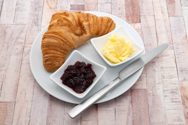 Breakfast items of a fresh croissant with dairy butter and raspberry jam