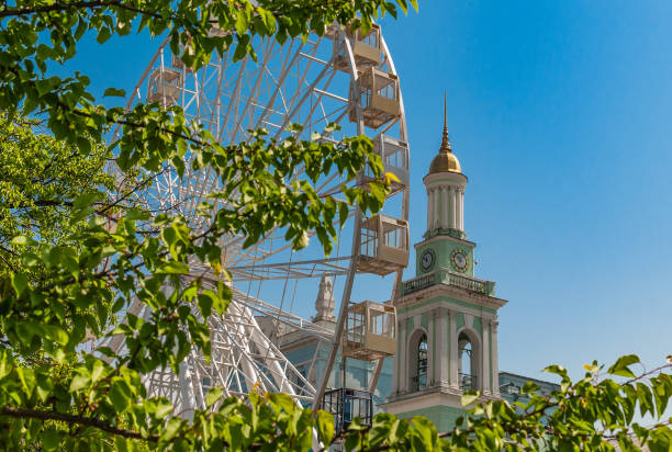 istock Amusement park with ferris wheel and green trees on blue sky background 1472169577