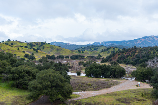 Malibu Creek State Park muddy after a large rainfall in southern California. Streams overflowing, lush green grass, large oak trees, clouds, dam rushing, water flowing.