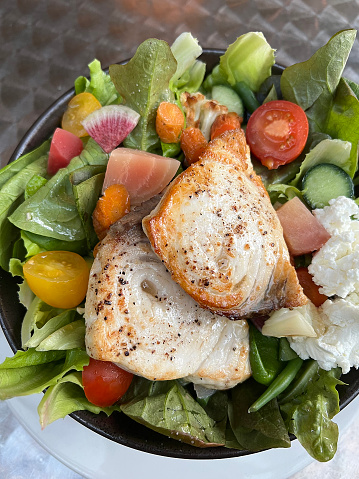 Two grilled swordfish steaks on top of a fresh green salad with tomatoes, radishes, and goat cheese.
