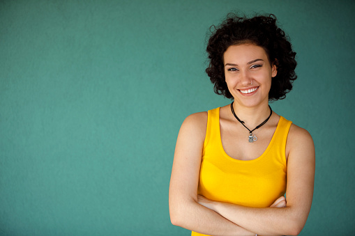 Portrait of confident young woman with arms crossed against green wall