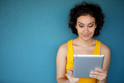 Young smiling woman using digital tablet against blue background