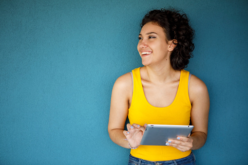 Young smiling woman looking away and using digital tablet against blue background
