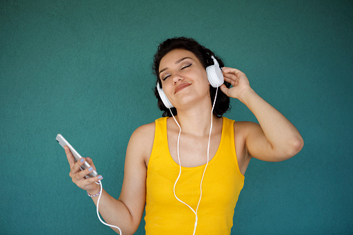 Woman with headphones listening to music on smart phone against green background