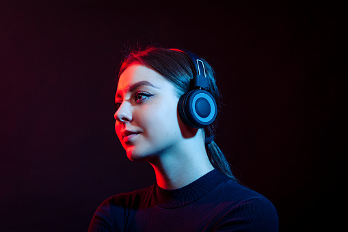 Studio portrait of a happy young white woman listening to music with wireless headphones