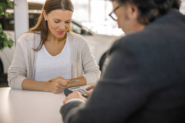 istock Female is smiling while paying a new car with her credit card using a credit card reader,sitting together with a car salesman,at an office table at a car dealer 1472176021