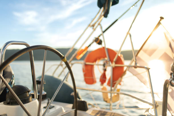 Alone young man at the helm while sailing on sailboat wearing a black sweatshirt. Beautiful sunny day with sunset in background