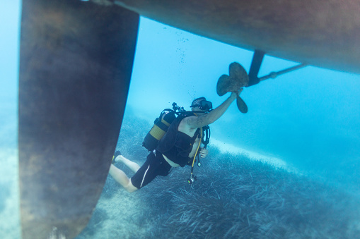 Underwater shot of scuba diver examining and checking propeller and hull of sailboat