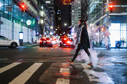 Woman in her 30s walking down the streets in Manhattan, New York, at night.