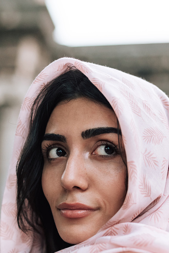 Female portrait of beautiful muslim woman who wear pink headscarf like hijab. Lifestyle photography of nice oriental people. Girl is brunette with dark skin and brown eyes. Person wearing in arabic style