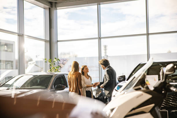 biznesmen daje klucze klientce, obie uśmiechają się do siebie, kobieta stoi z przodu, wieczorem w salonie samochodowym - professional dealer zdjęcia i obrazy z banku zdjęć