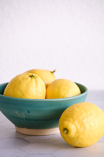 Three lemons in a turquoise bowl with a light background.