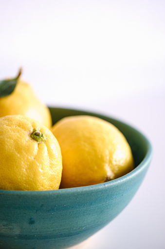 Three lemons in a turquoise bowl with a light background.