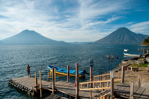 A man stands at the end of a dock in front of two volcanoes at Lake Atitlan, Guatemala