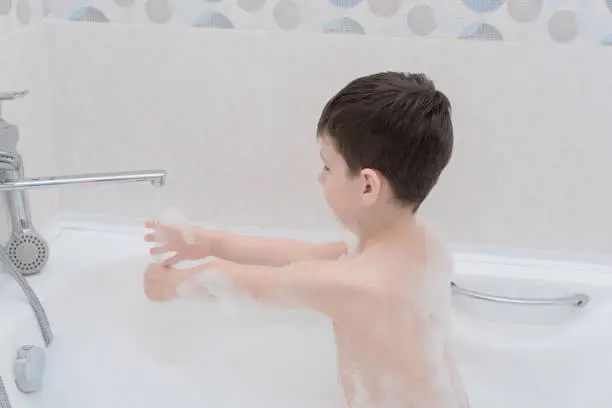 Photo of Happy boy takes a bath with lush foam playing with bubbles. Personal hygiene, healthcare concept