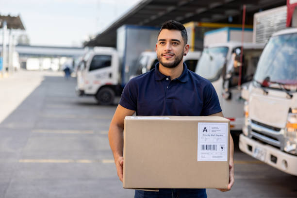 istock Man working at a distribution warehouse and carrying a box towards a truck 1472189901