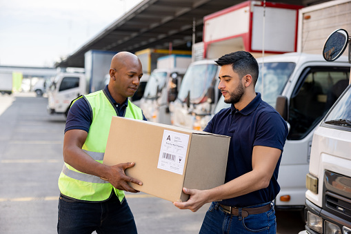 Men working at a distribution warehouse and carrying a box towards a truck