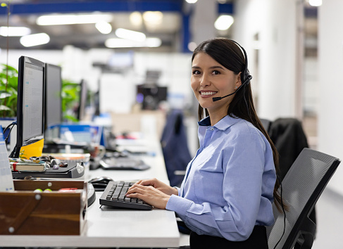 Happy female customer service representative working at a call center and looking at the camera smiling