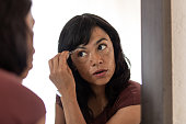 Woman tweezing eyebrows in front of mirror