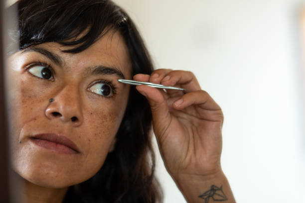 Woman tweezing eyebrows in front of mirror
