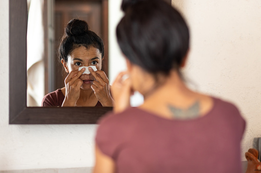 Woman applying pore strips on nose in bathroom