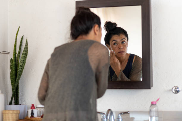 istock Woman cleansing face looking into bathroom mirror 1472202512