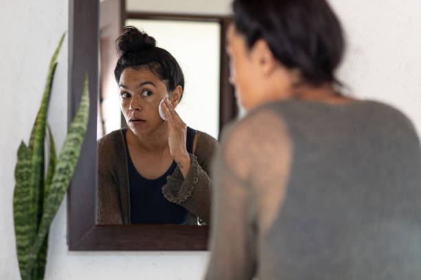 istock Woman cleansing face looking into bathroom mirror 1472202556