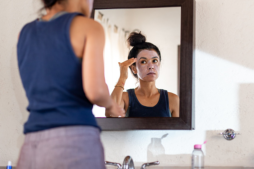 Woman applying white sunblock to face, looking at
 bathroom mirror