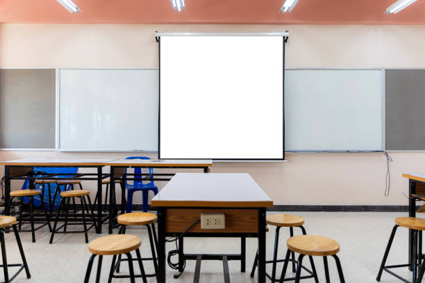 istock Projector screen canvas in modern conference room with big windows. Side view.Empty classroom or presentation room interior with desks 1472203697