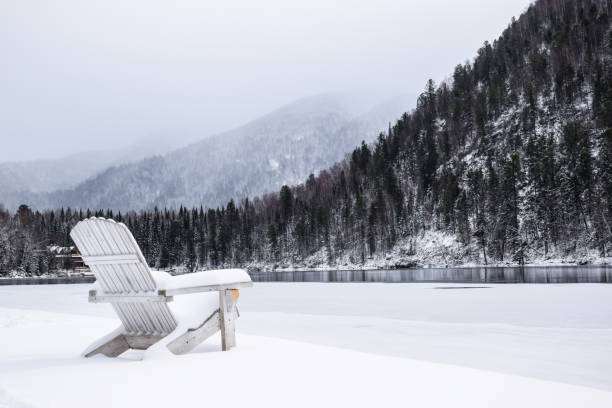 une station balnéaire sur le lac en hiver. des chaises en bois dans la neige au bord d’un lac gelé. une chaise en bois dans la neige au bord du lac sur fond de montagnes. - nobody tranquil scene nature park photos et images de collection