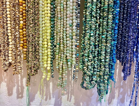 Horizontal still life of a variety of crystal strings hanging in bead shop, in blue turquoise pink green and earth colours awaiting selection at market stall to make handmade jewellery Byron Bay Australia