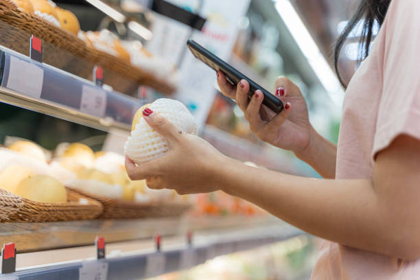 una joven compra comestibles en un supermercado con un teléfono en las manos. alimentos saludables. teléfono inteligente de mano para escanear el código qr - presencia internacional alimentaria  fotografías e imágenes de stock