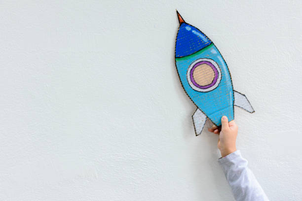 istock Young Asian boy holding rocket on raised hand standing in art class in backlit with imagination the astronaut and space rocket 1472208300