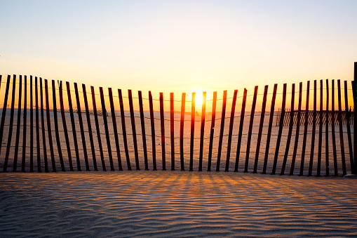 Sun goes down behind a wooden fence at the beach, yellow sun hits the horizon, soft warm colors fill the sky.