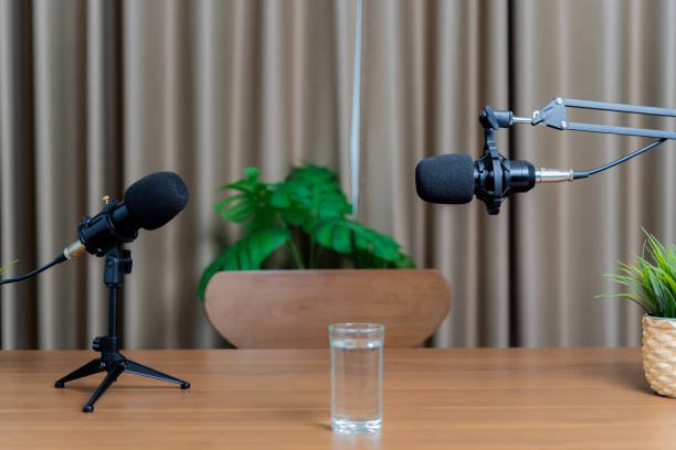 istock Two microphones for conversing, preparing to talk in a studio. A glass of water placed on a wooden table for hosts. 1472209366
