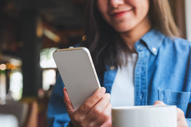 istock Closeup image of a young woman holding and using mobile phone while drinking coffee in cafe 1472211536