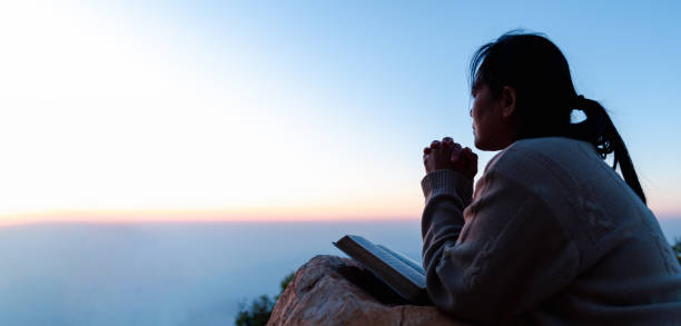 Silhouette of woman kneeling down praying for worship God at sky background. Christians pray to jesus christ for calmness. In morning people got to a quiet place and prayed. Banner with copy space. stock photo