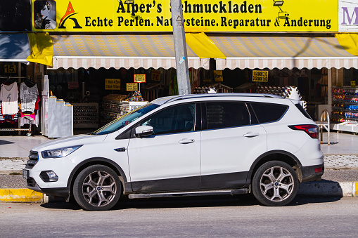Side, Turkey -January 23, 2023:   white Ford Kuga   is parked  on the street on a warm  day against the backdrop of a house , shops