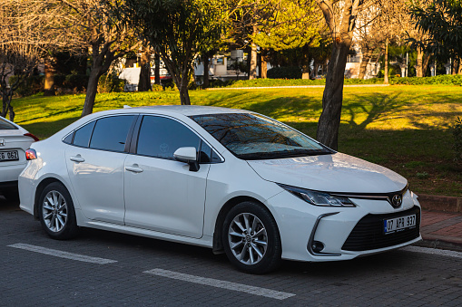 Side; Turkey – January 24 2023:     white Toyota Corolla   is parked  on the street on a warm  day against the backdrop of a park