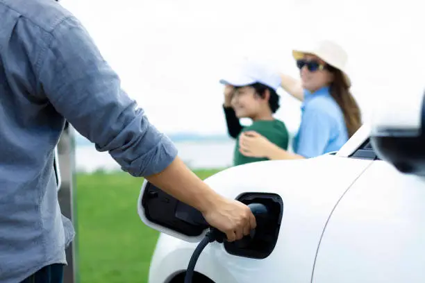 Concept of progressive happy family enjoying their time at green field and lake with electric vehicle. Electric vehicle driven by clean renewable from eco-friendly power sauce.